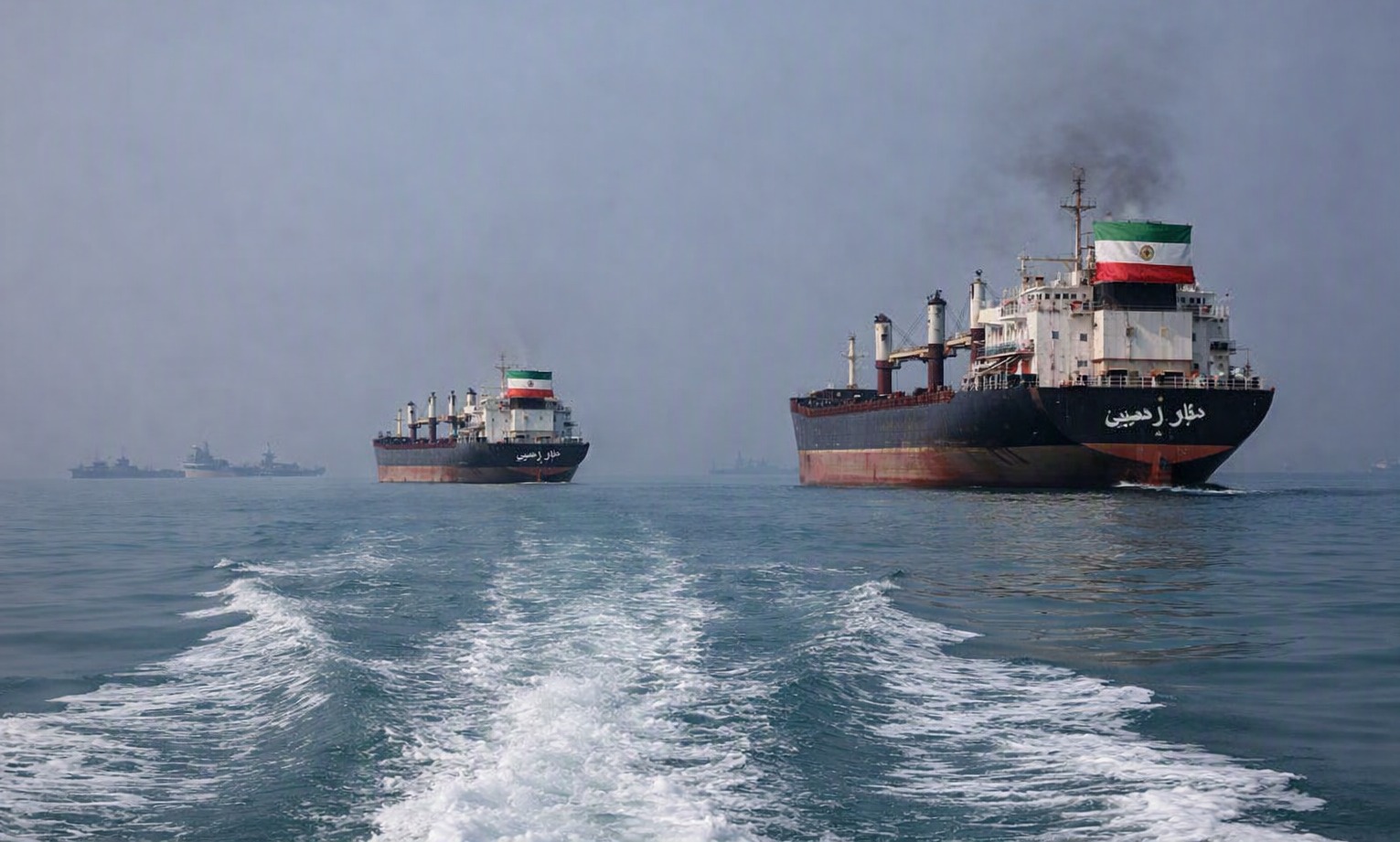 Iranian cargo ships navigating the Strait of Hormuz with distant US Navy vessels under tense skies